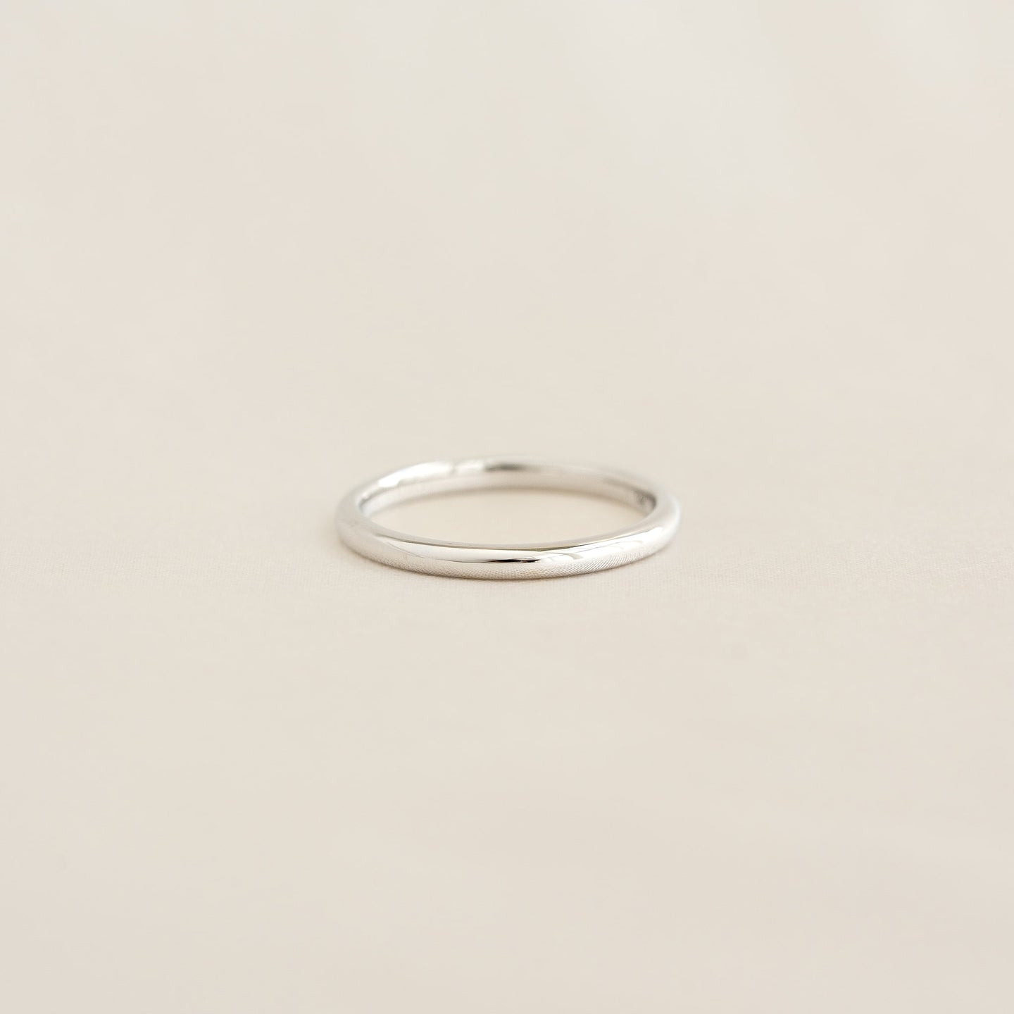 Close-up of the Round White Gold Band - Marni, a slim 2mm polished ring on a soft beige surface