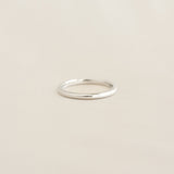 Close-up of the Round White Gold Band - Marni, a slim 2mm polished ring on a soft beige surface
