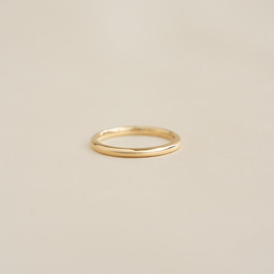 Close-up of a Round 14k Gold Band - Marni resting on a smooth beige surface with soft lighting