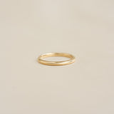 Close-up of a Round 14k Gold Band - Marni resting on a smooth beige surface with soft lighting