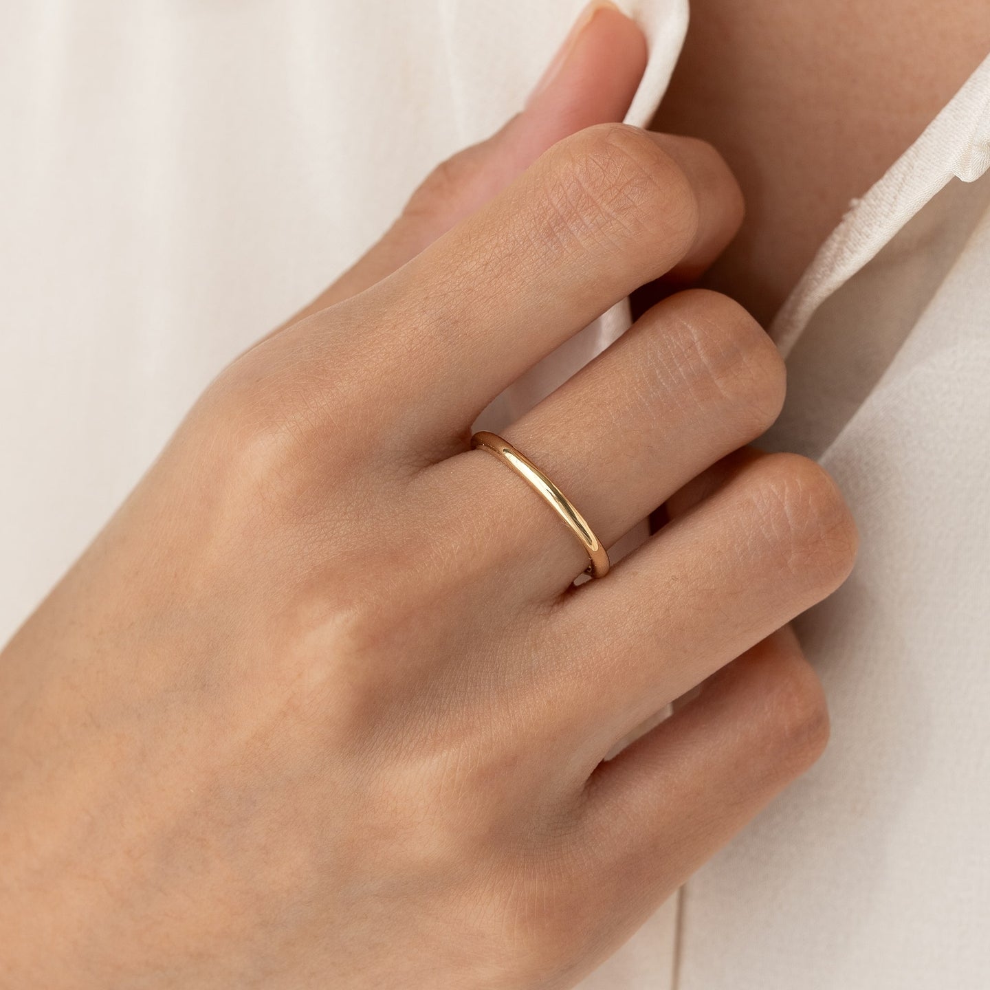 Close-up of a hand wearing the Round 14k Gold Band - Marni on the ring finger against a neutral background