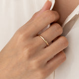 Close-up of a hand wearing the Round 14k Gold Band - Marni on the ring finger against a neutral background