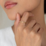 Close-up of a hand wearing the Round 14k Gold Band - Marni on the ring finger against a soft neutral background