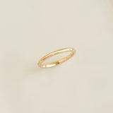 Close-up of the Round 14k Gold Band - Marni showcasing its slim, polished gold surface on a neutral beige background