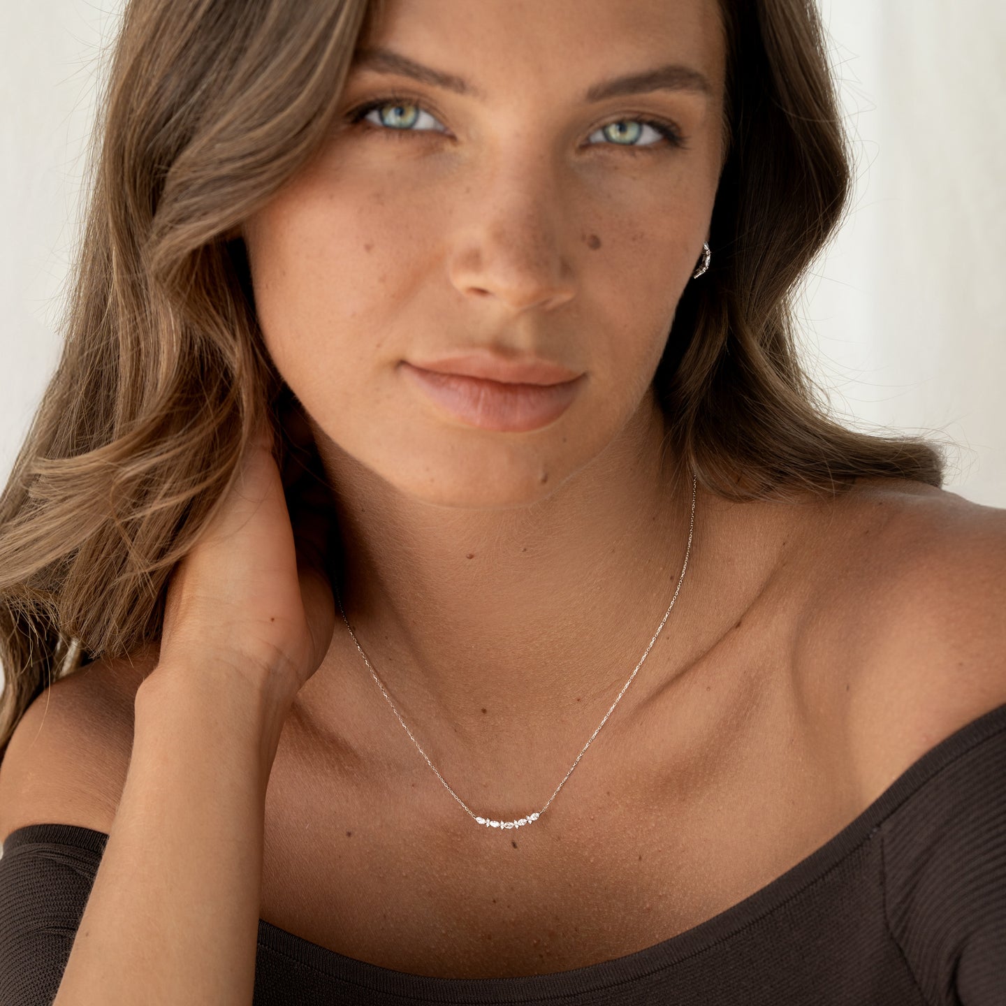 Close-up of a woman wearing the Marquise and Round Diamond Necklace White Gold - Noelia with natural light and a dark off-shoulder top