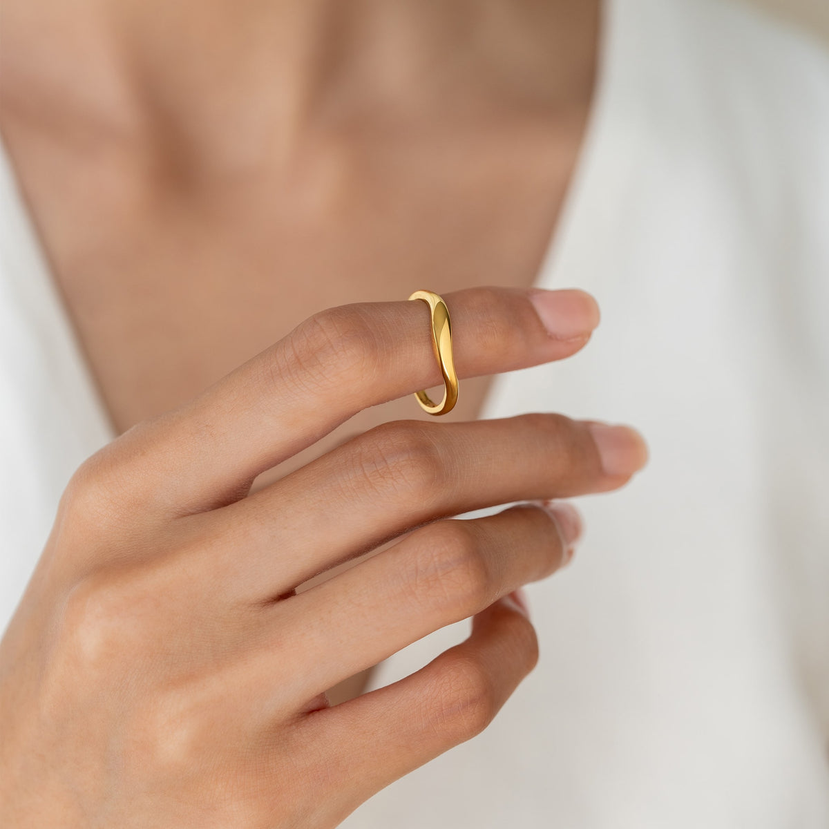 Close-up of a hand wearing the gold vermeil Organic Wavy Ring - Nyssa against a soft white fabric background