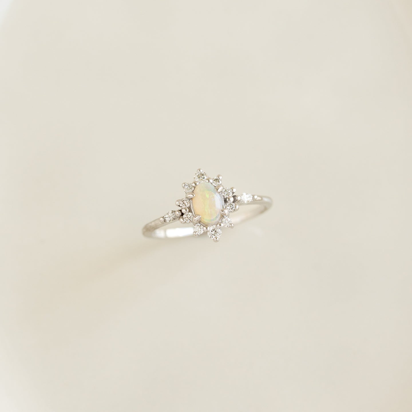 Close-up of Sunburst Opal Halo Ring White Gold - Solana with opal cabochon and diamond halo on a soft beige background
