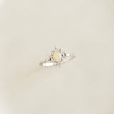 Close-up of Sunburst Opal Halo Ring White Gold - Solana with opal cabochon and diamond halo on a soft beige background