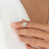 Close-up of hand wearing Sunburst Opal Halo Ring White Gold - Solana with opal and diamond halo on light background