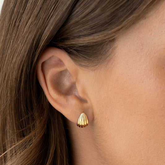 Close-up of an ear wearing Scalloped Huggie Earrings - Tulisa in gold vermeil with shell-inspired design