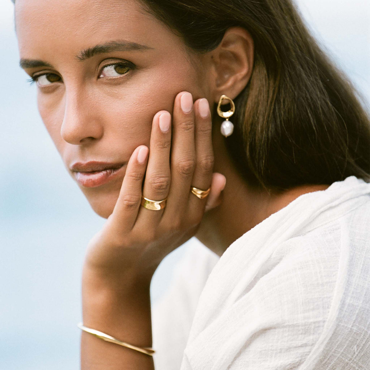 Close-up of a woman wearing the Wide Organic Ring - Essie and gold jewelry with neutral makeup and white top