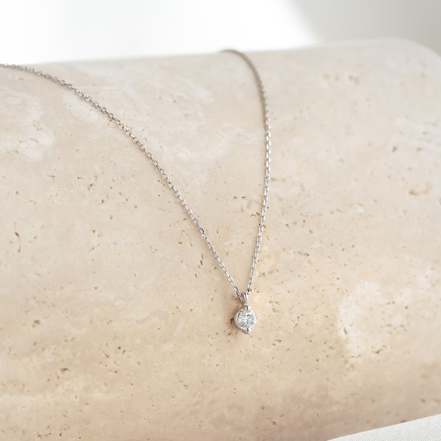 Close-up of a Diamond Pendant Necklace White Gold - Atiana featuring a round diamond on a delicate white gold chain against beige background