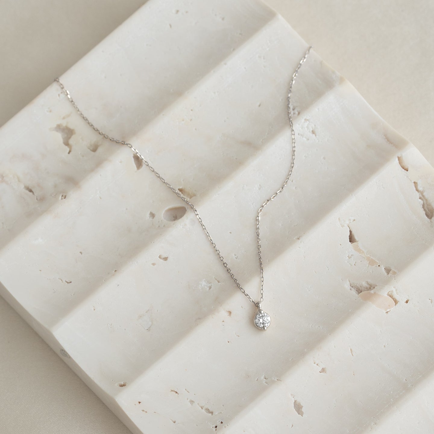 Close-up of a delicate Diamond Pendant Necklace White Gold - Atiana resting on a textured light stone surface