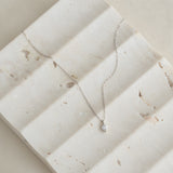Close-up of a delicate Diamond Pendant Necklace White Gold - Atiana resting on a textured light stone surface