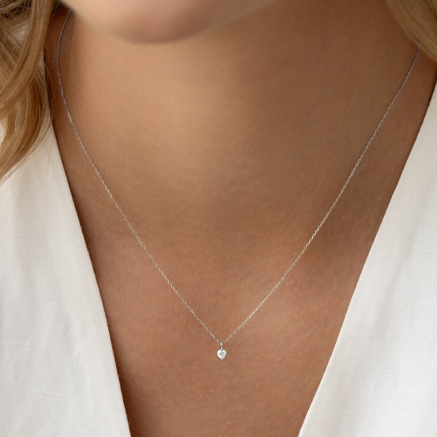Close-up of a woman wearing the Diamond Pendant Necklace White Gold - Atiana with a single round diamond on a delicate chain