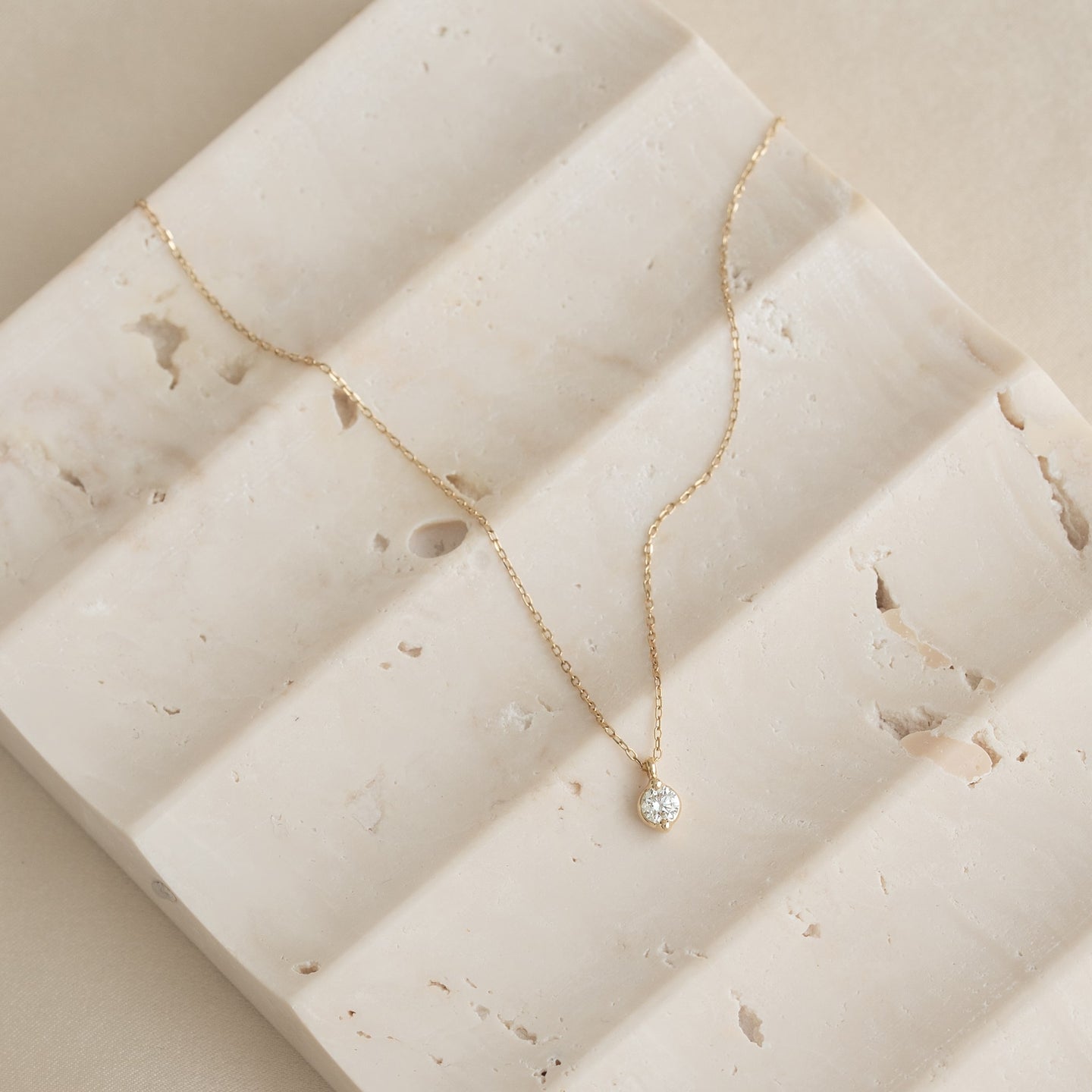 Close-up of Diamond Pendant Necklace 14k Gold - Atiana displayed on textured beige stone surface with soft natural light