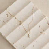 Close-up of Diamond Pendant Necklace 14k Gold - Atiana displayed on textured beige stone surface with soft natural light