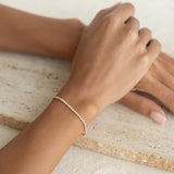Close-up of a wrist wearing the Tennis Bracelet - Audrey with sparkling cubic zirconia stones on a neutral stone surface