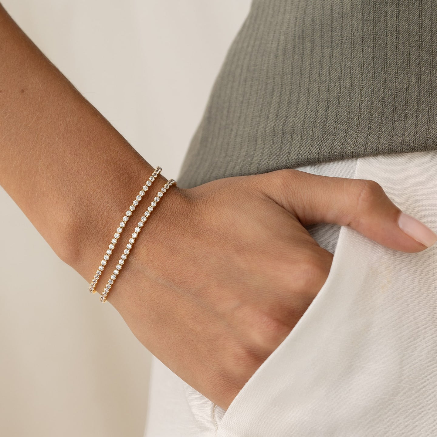 Close-up of a wrist wearing two delicate Tennis Bracelet - Audrey bracelets with sparkling stones against a neutral background