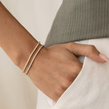 Close-up of a wrist wearing two delicate Tennis Bracelet - Audrey bracelets with sparkling stones against a neutral background