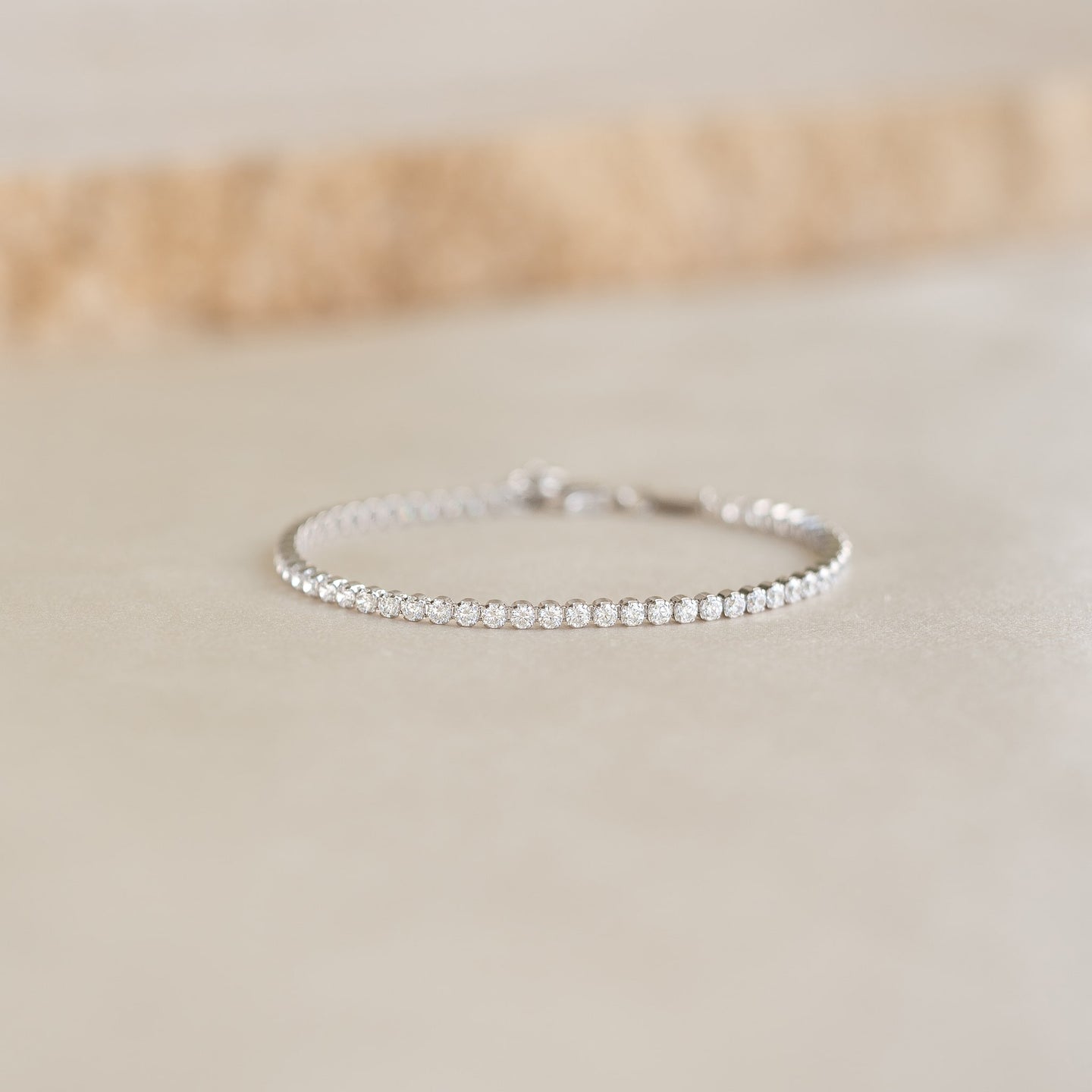 Close-up of Tennis Bracelet Silver - Audrey featuring sparkling cubic zirconia stones on a sterling silver chain resting on a beige surface