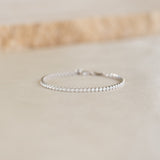 Close-up of Tennis Bracelet Silver - Audrey featuring sparkling cubic zirconia stones on a sterling silver chain resting on a beige surface