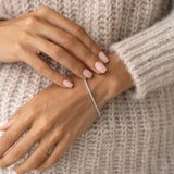 Close-up of a woman’s wrist wearing the Tennis Bracelet Silver - Audrey with cubic zirconia stones and a beige knit sweater background