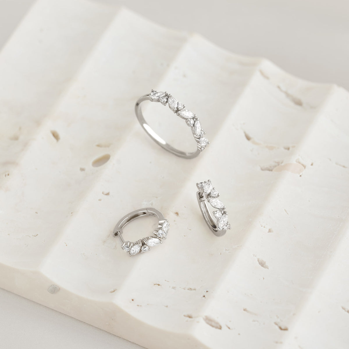 Close-up of Marquise and Round Diamond Huggie Earrings White Gold - Rosa displayed on textured white stone surface