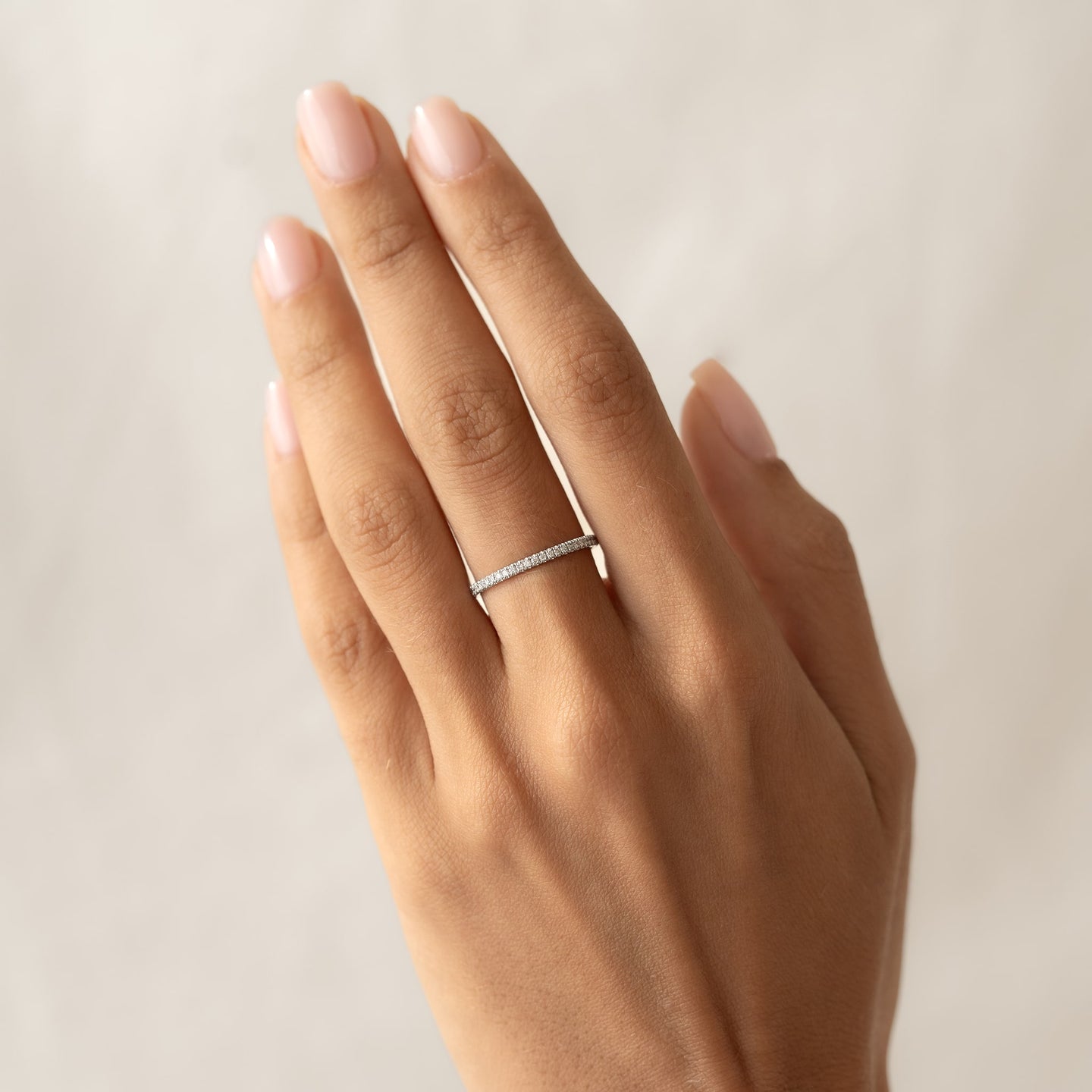 Close-up of a hand wearing a Diamond Eternity Ring White Gold with a circle of sparkling diamonds on a neutral background