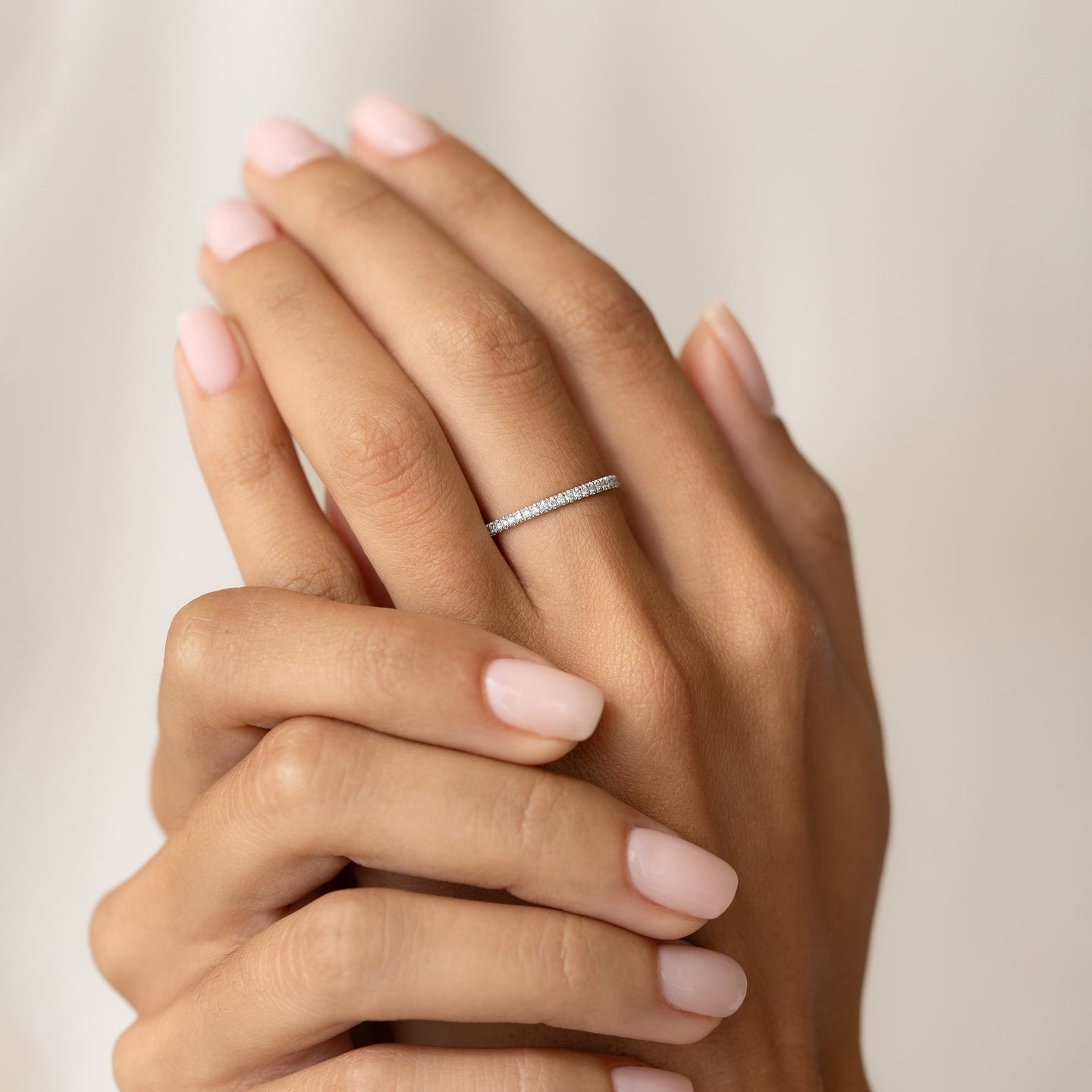 Close-up of hands wearing a Diamond Eternity Ring White Gold with lab-grown diamonds on a neutral background