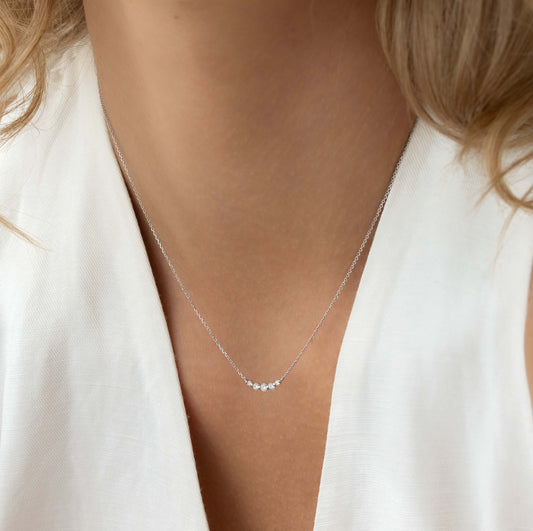 Close-up of a woman wearing the Diamond Curved Bar Necklace White Gold - Elodie with five graduated diamonds on a delicate chain