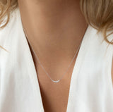 Close-up of a woman wearing the Diamond Curved Bar Necklace White Gold - Elodie with five graduated diamonds on a delicate chain