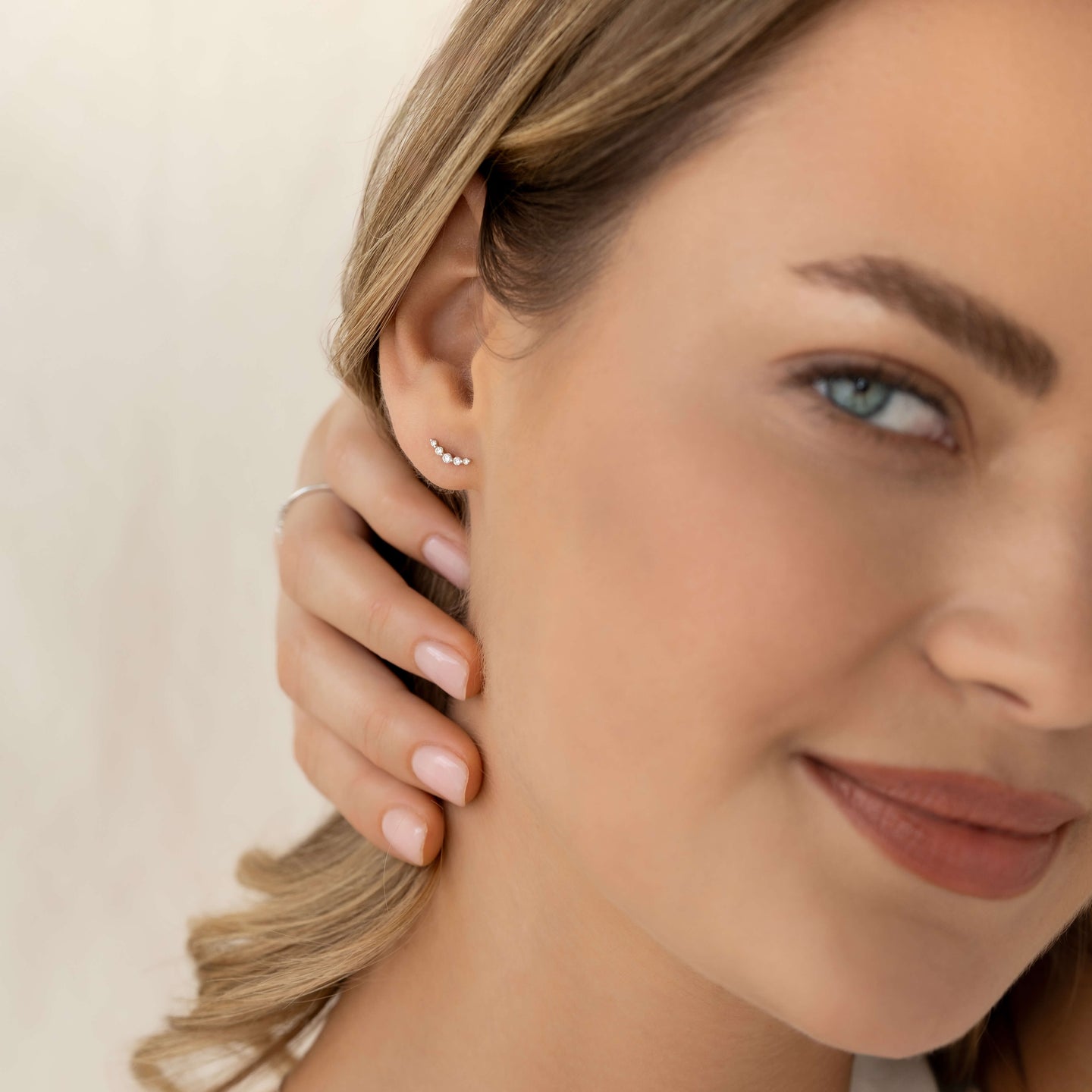 Close-up of a woman wearing Diamond Climber Stud Earrings White Gold - Rhea with natural makeup and hand near her ear