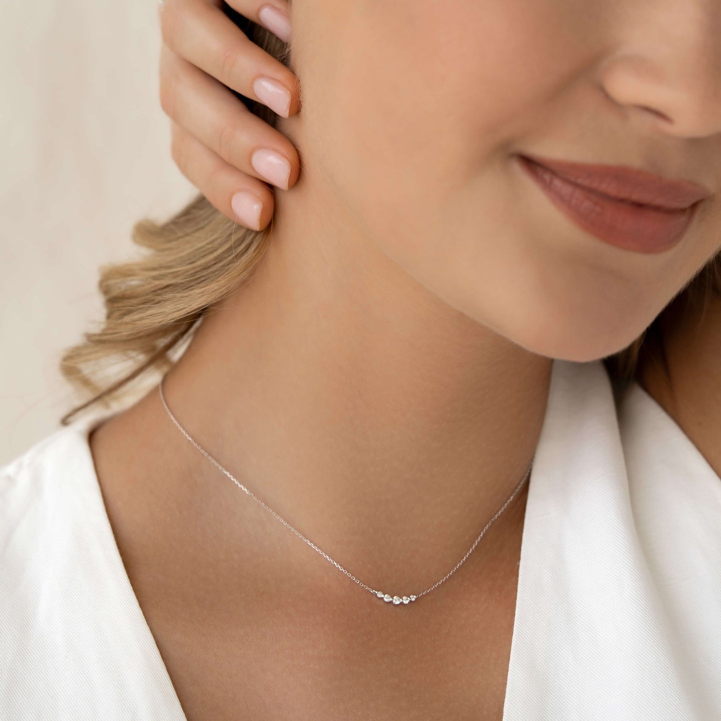 Close-up of a woman wearing the Diamond Curved Bar Necklace White Gold - Elodie with five graduated diamonds on a delicate chain