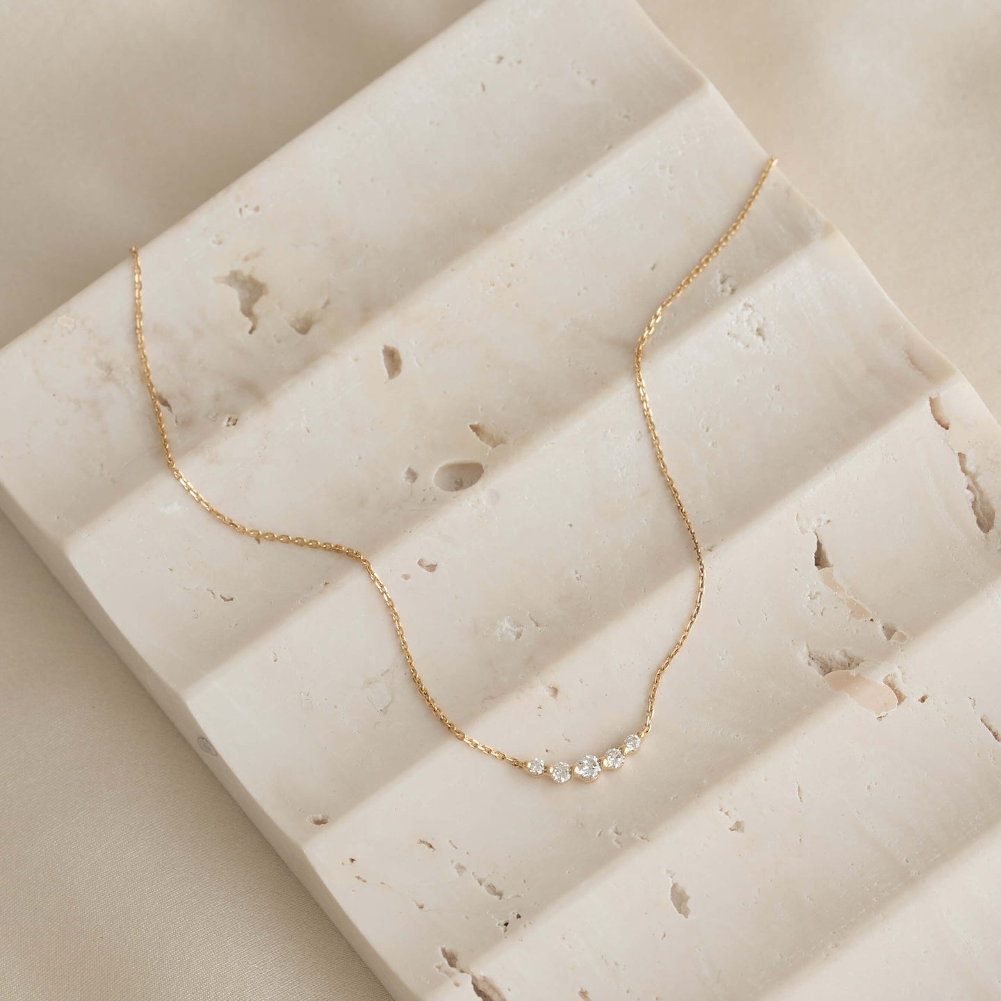 Close-up of Diamond Curved Bar Necklace 14k Gold - Elodie with five graduated diamonds on a textured stone surface