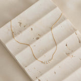 Close-up of Diamond Curved Bar Necklace 14k Gold - Elodie with five graduated diamonds on a textured stone surface