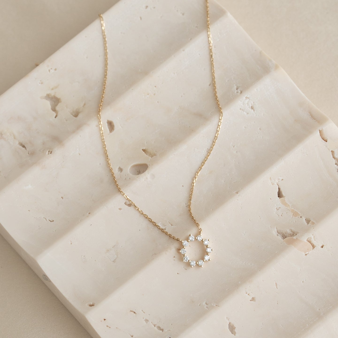Close-up of Diamond Sun Necklace 14k Gold - Leda with sparkling diamonds on a delicate gold chain resting on textured stone