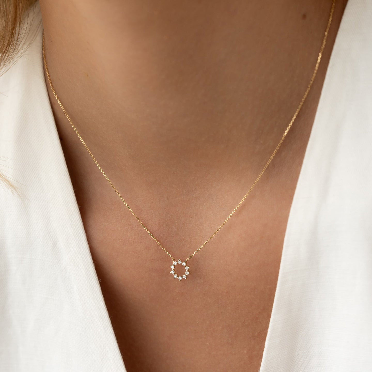 Close-up of a woman wearing the Diamond Sun Necklace 14k Gold - Leda with a delicate diamond sun pendant on a gold chain
