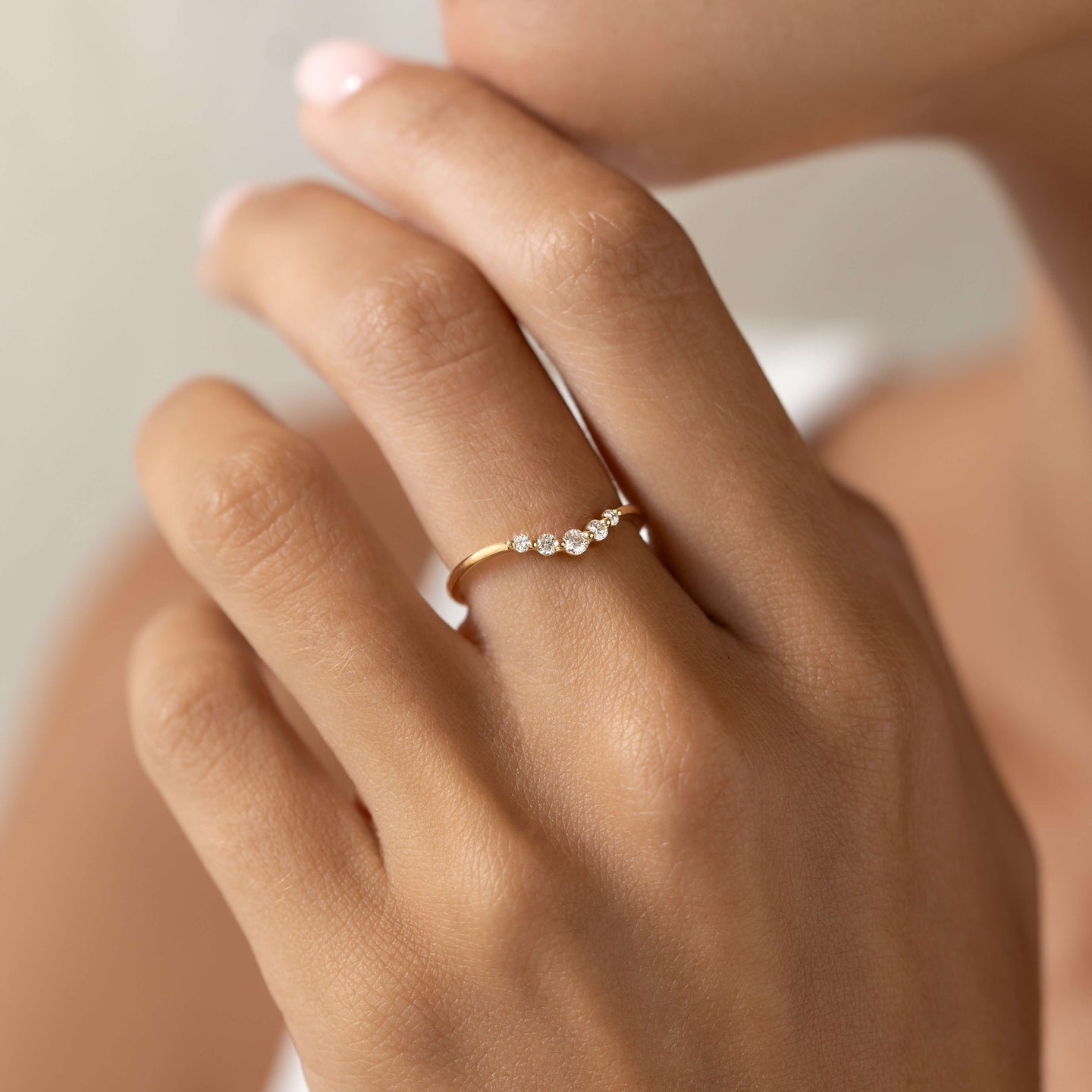 Close-up of a hand wearing the Graduated Diamond V Ring 14k Gold - Liora with five sparkling diamonds on a gold band