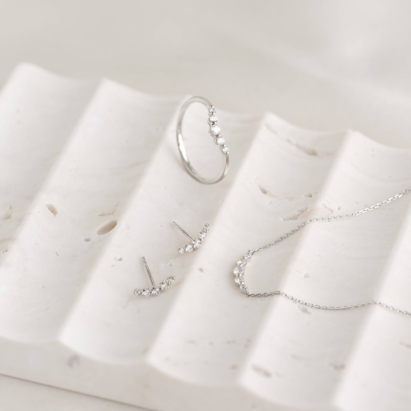 Close-up of Diamond Climber Stud Earrings White Gold - Rhea with matching white gold ring and necklace on a textured white surface