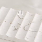 Close-up of Diamond Climber Stud Earrings White Gold - Rhea with matching white gold ring and necklace on a textured white surface