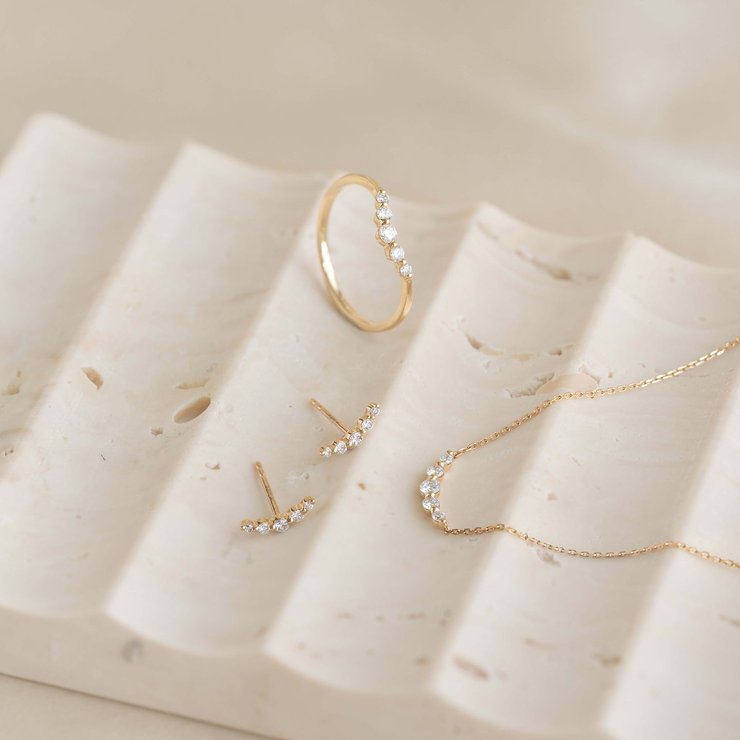 Close-up of Diamond Curved Bar Necklace 14k Gold - Elodie with matching curved bar earrings and ring on beige stone surface