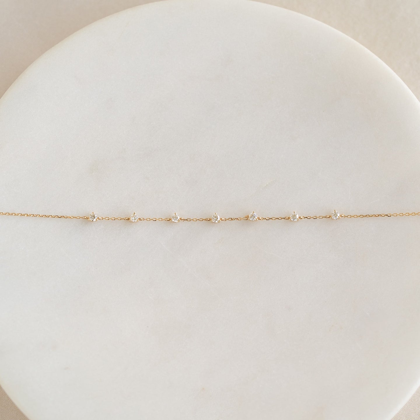 Close-up of Diamond Bracelet 14k Gold - Lyra with seven small diamonds on delicate gold chain on a white marble surface