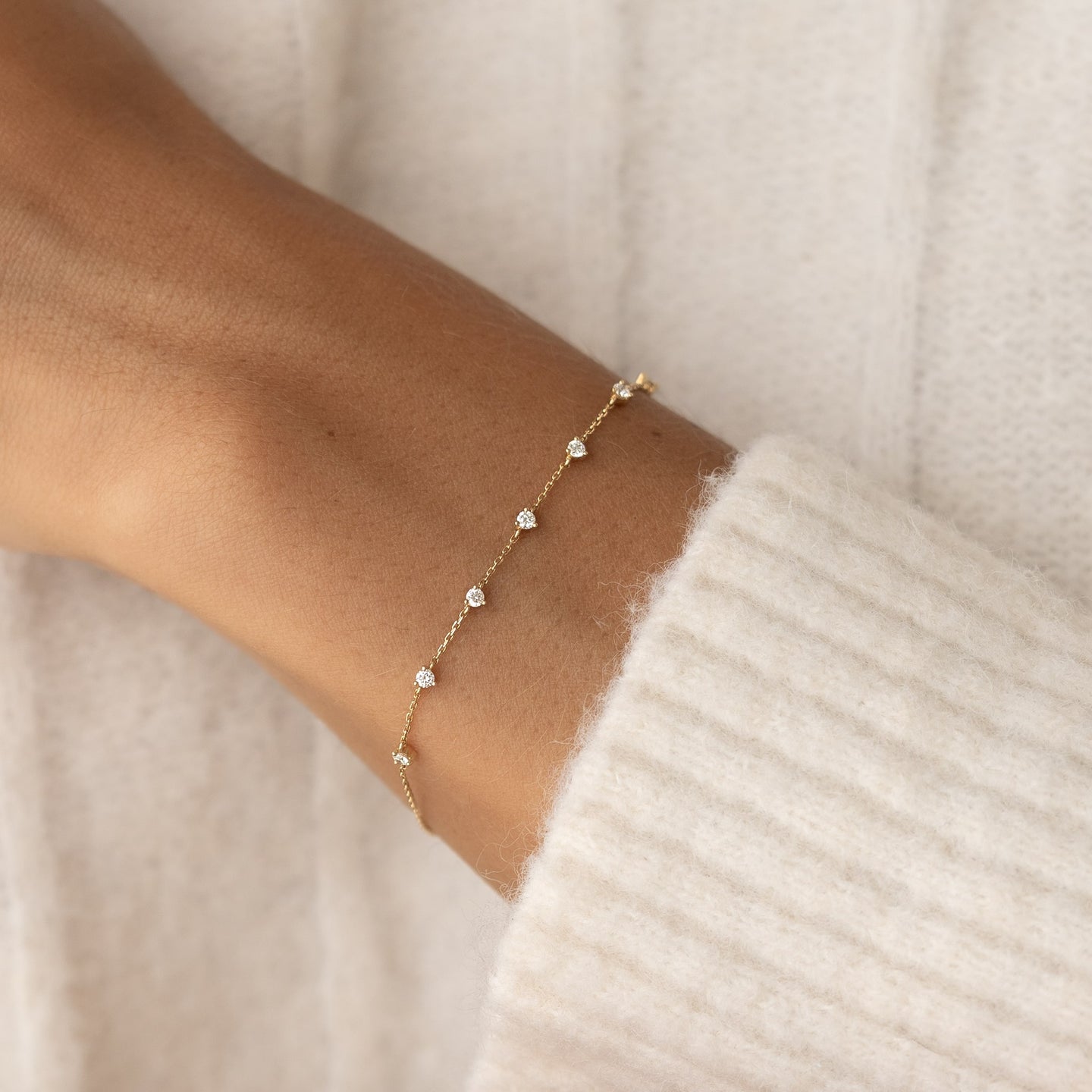 Close-up of a wrist wearing the Diamond Bracelet 14k Gold - Lyra with seven round diamonds on a thin gold chain
