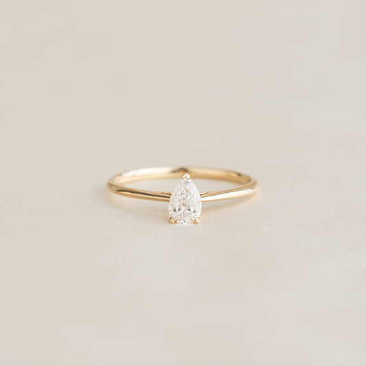 A delicate Gold ring with a pear-shaped diamond set on a soft beige background, exuding elegance and simplicity.