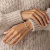 Close-up of a wrist wearing the Diamond Tennis Bracelet White Gold (1.501 ct tw) - Mirella against a beige sweater background