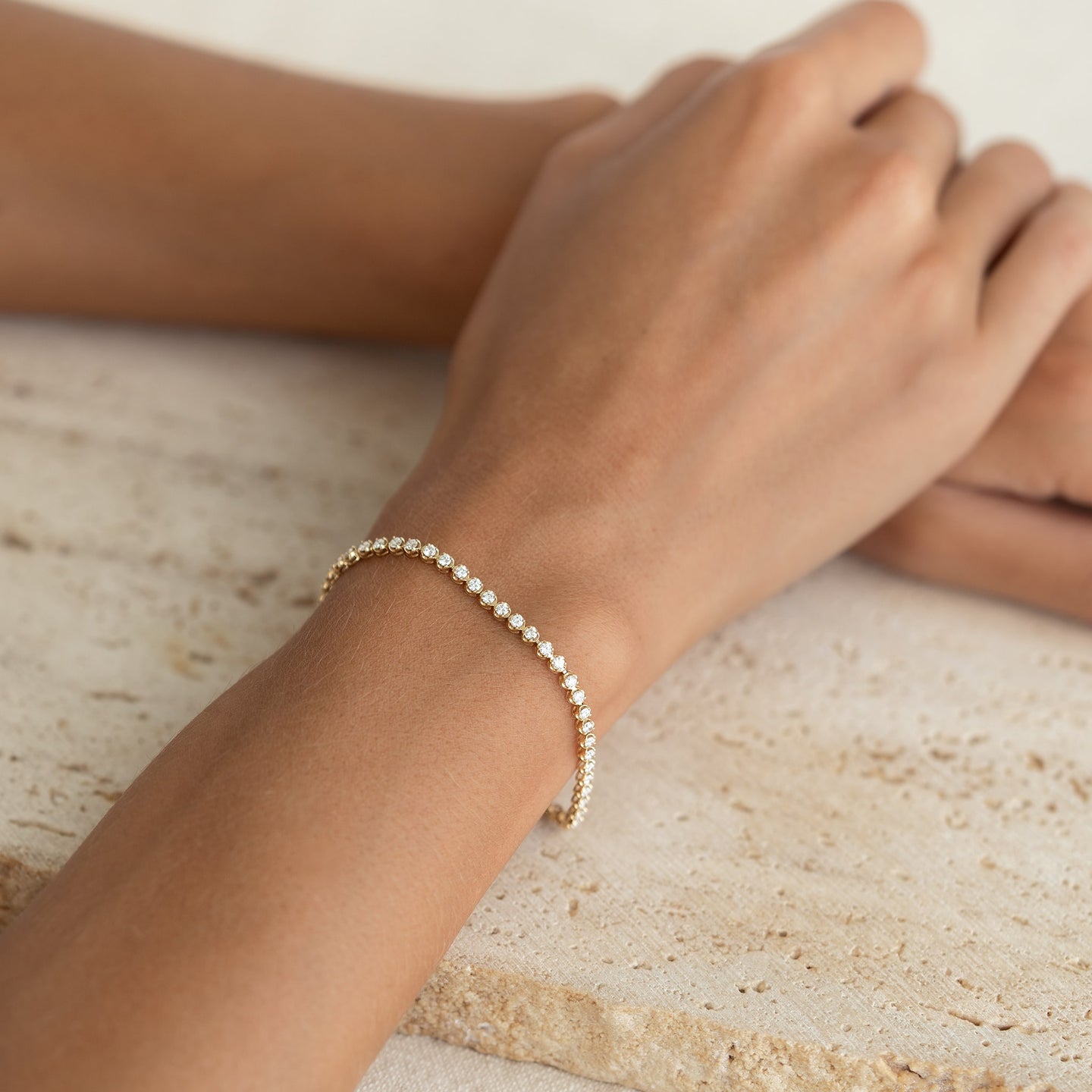 Close-up of wrist wearing Diamond Tennis Bracelet 14k Gold (1.62 ct tw) - Mirella resting on textured stone surface