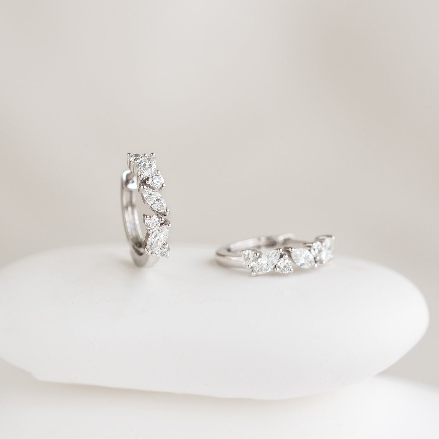 Close-up of Marquise and Round Diamond Huggie Earrings White Gold - Rosa displayed on a smooth white surface with soft background