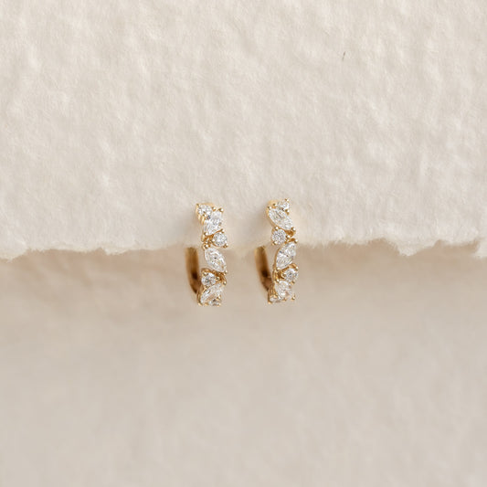 Close-up of Marquise and Round Diamond Huggie Earrings 14k Gold - Rosa with floral diamond design on beige textured background