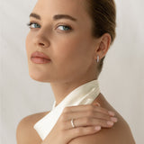 Close-up of a woman wearing Marquise and Round Diamond Huggie Earrings White Gold - Rosa with a white halter top background